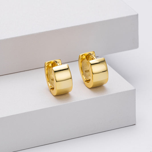 Gold hoop earrings on a white surface with a light gray background