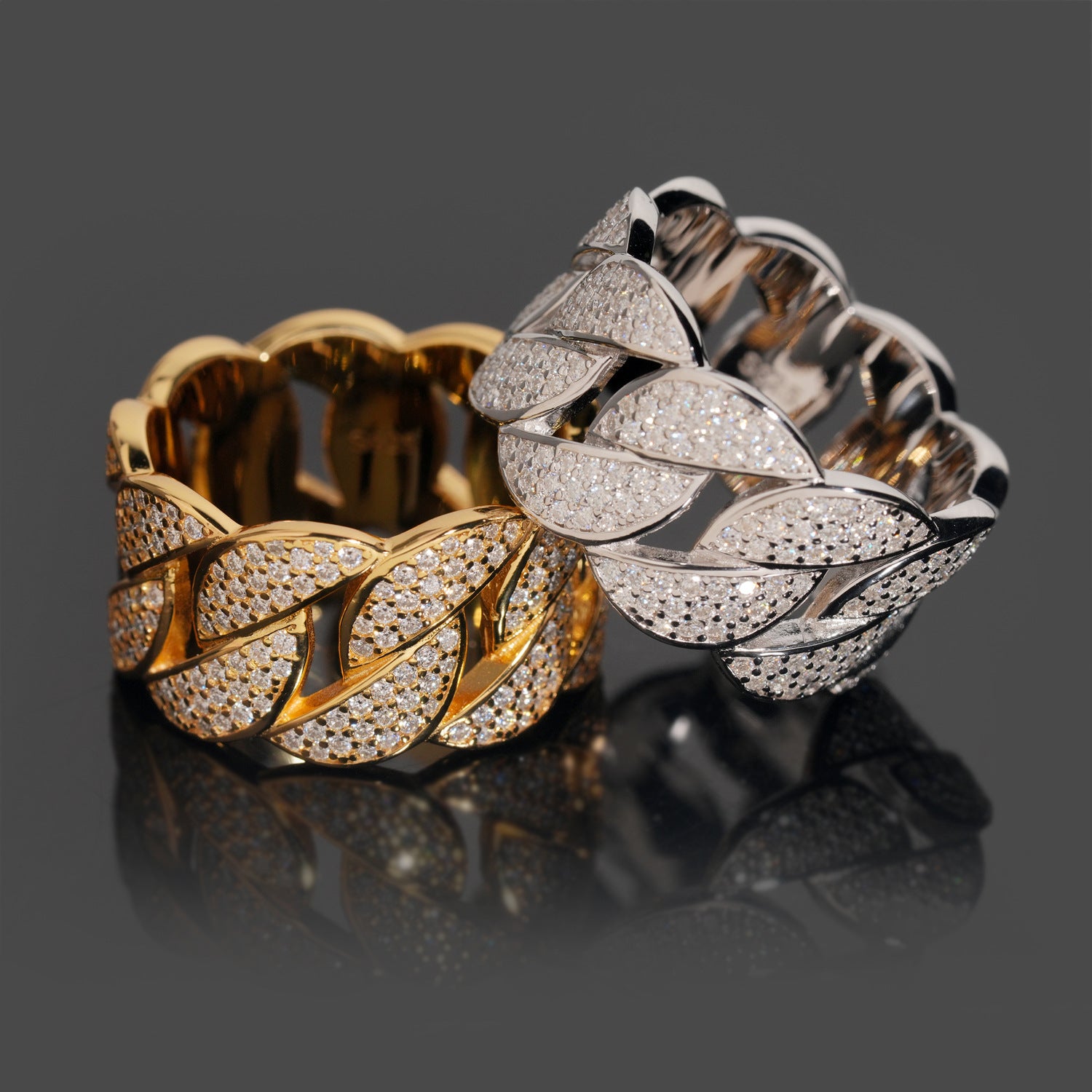 Two gold and silver leaf-patterned rings on a reflective surface with a dark background