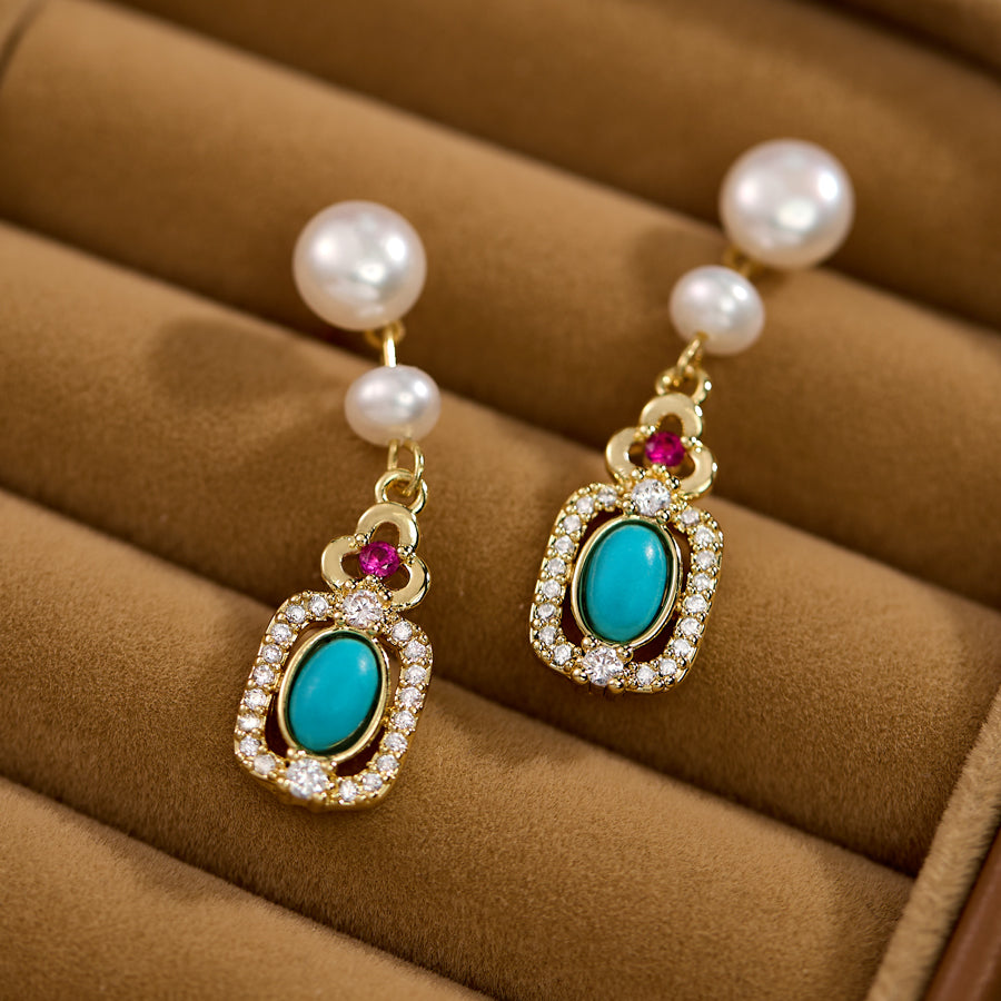 Pearl earrings with turquoise and red gemstones on a brown surface