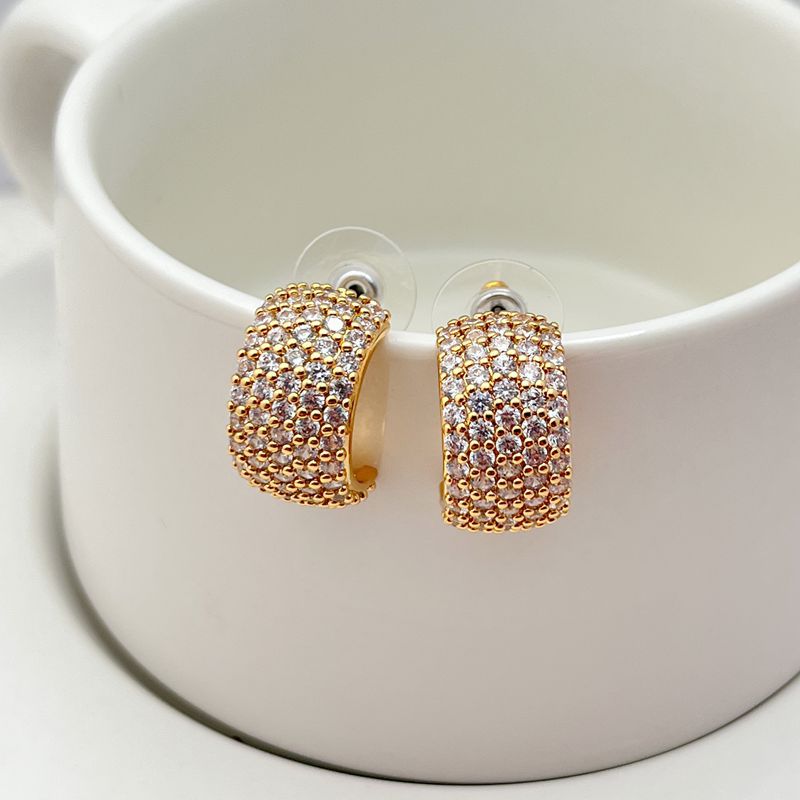 Gold-tone huggie hoops fully pavé-set with crystals on a soft white or champagne background. Alt: “Kate Spade Brilliant Statements Gold Pavé Huggies – Full Crystal Hoop Earrings.”
