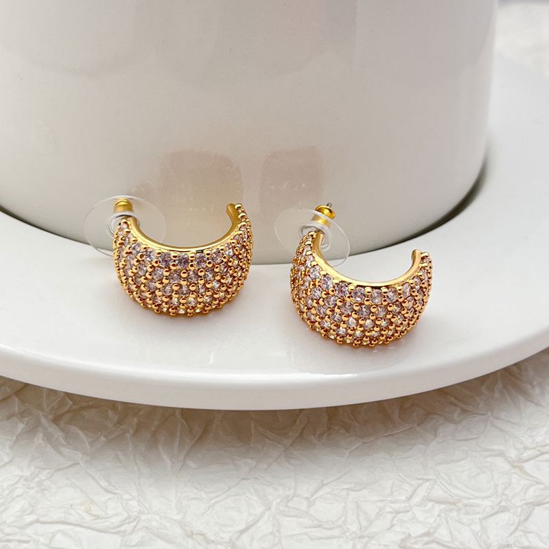 Gold-tone huggie hoops fully pavé-set with crystals on a soft white or champagne background. Alt: “Kate Spade Brilliant Statements Gold Pavé Huggies – Full Crystal Hoop Earrings.”