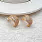 Gold-tone huggie hoops fully pavé-set with crystals on a soft white or champagne background. Alt: “Kate Spade Brilliant Statements Gold Pavé Huggies – Full Crystal Hoop Earrings.”