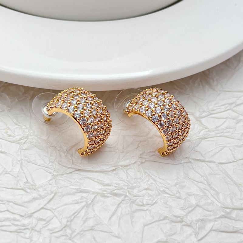 Gold-tone huggie hoops fully pavé-set with crystals on a soft white or champagne background. Alt: “Kate Spade Brilliant Statements Gold Pavé Huggies – Full Crystal Hoop Earrings.”