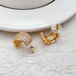 Gold-tone huggie hoops fully pavé-set with crystals on a soft white or champagne background. Alt: “Kate Spade Brilliant Statements Gold Pavé Huggies – Full Crystal Hoop Earrings.”
