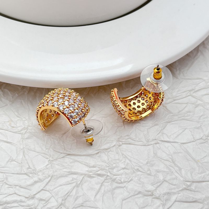 Gold-tone huggie hoops fully pavé-set with crystals on a soft white or champagne background. Alt: “Kate Spade Brilliant Statements Gold Pavé Huggies – Full Crystal Hoop Earrings.”