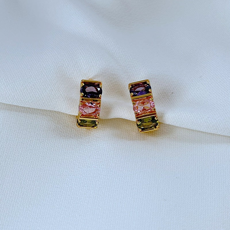 Earrings on a soft pastel pink or candy-striped background, showcasing the rainbow crystals along the gold hoop. Alt: “Kate Spade Candy Shop Small Stone Hoop Earrings – Rainbow Crystal Huggie Jewelry.”