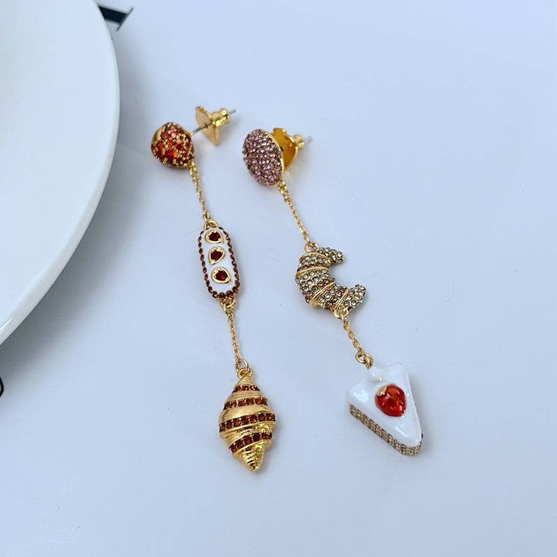  Earrings displayed side by side on a soft cream or café au lait background, showcasing the cherry shortcake and croissant charms. Alt: “Kate Spade Cherry Shortcake and Croissant Earrings – French Bakery Enamel Jewelry.”