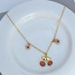 Necklace on a light, fresh background (white or soft green), highlighting the red and green enamel details. Alt: “Kate Spade Cherry and Flowers Necklace – Playful Botanical Charm Jewelry.”