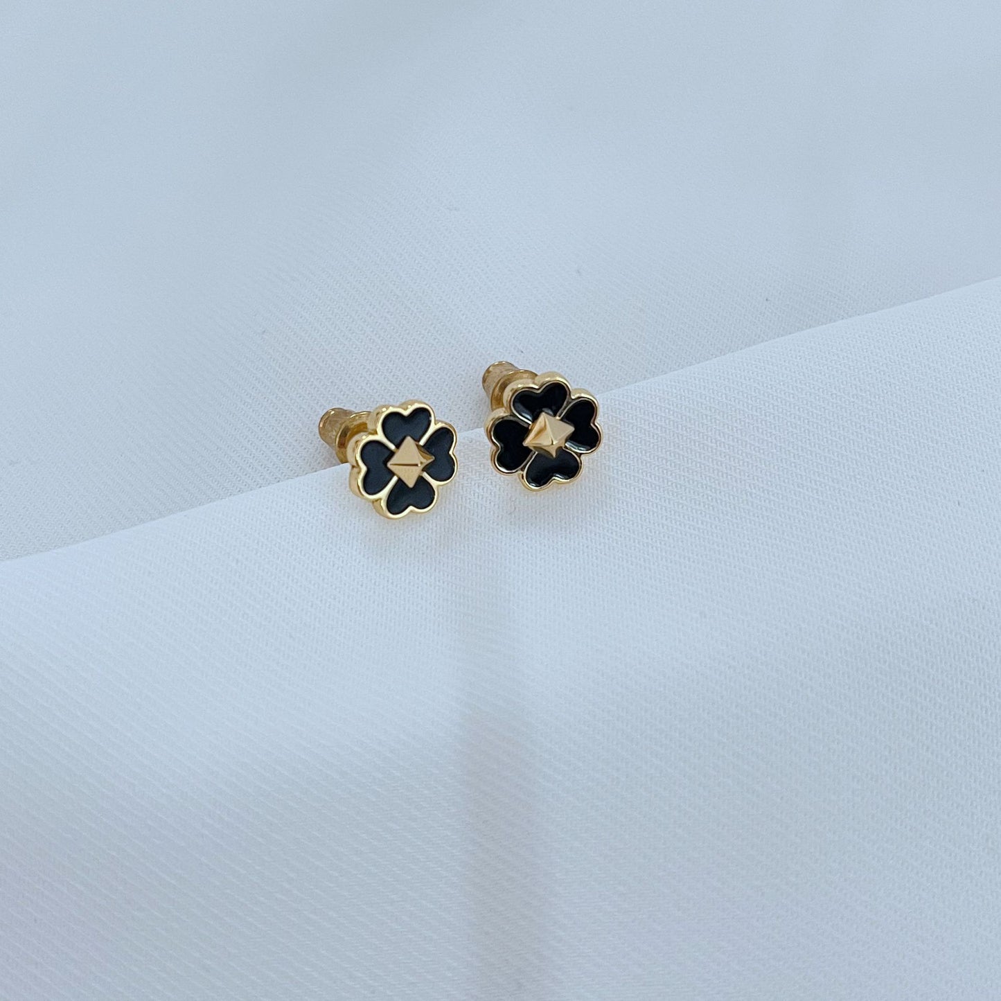 Clean, high-contrast shot of the necklace on a neutral background, highlighting the graphic interplay of gold and black on the clover.