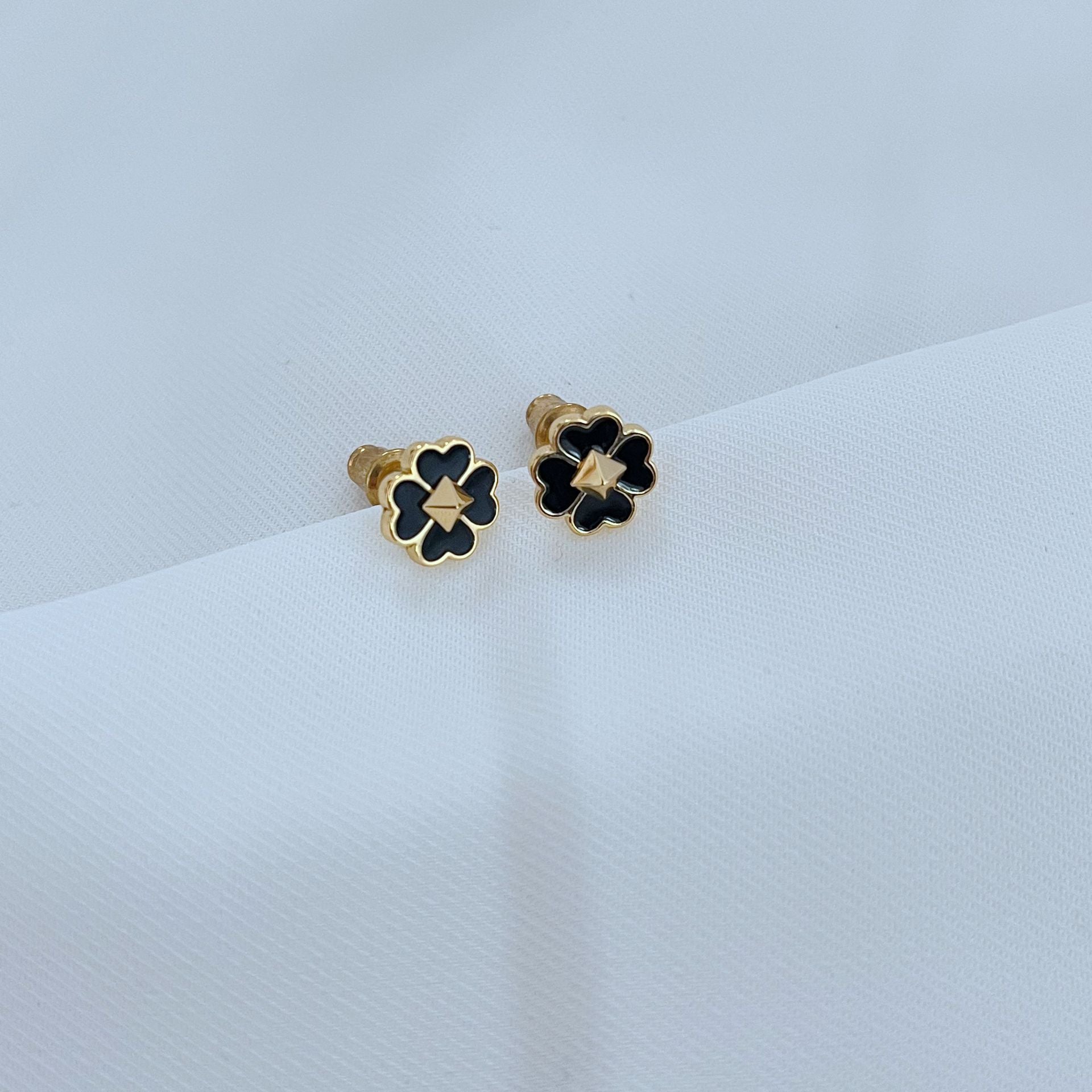 Clean, high-contrast shot of the necklace on a neutral background, highlighting the graphic interplay of gold and black on the clover.