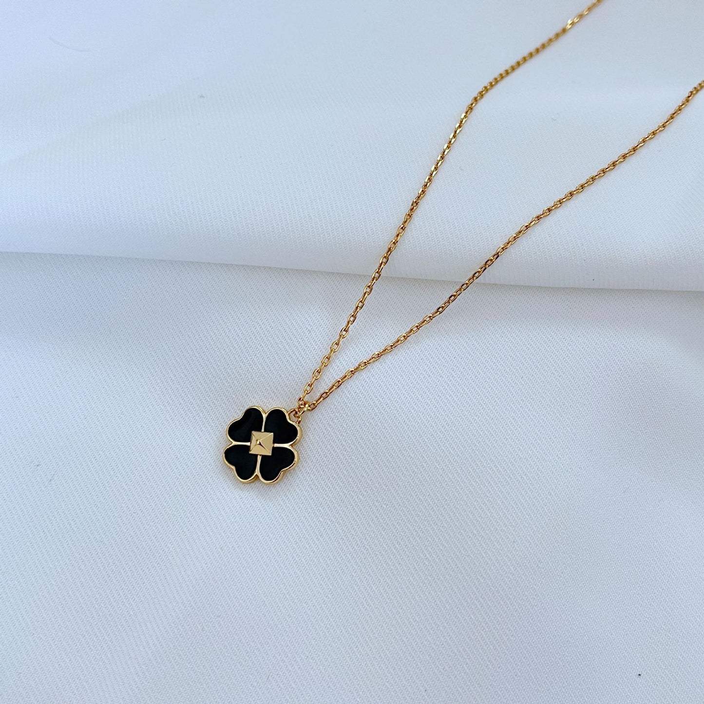 Clean, high-contrast shot of the necklace on a neutral background, highlighting the graphic interplay of gold and black on the clover.