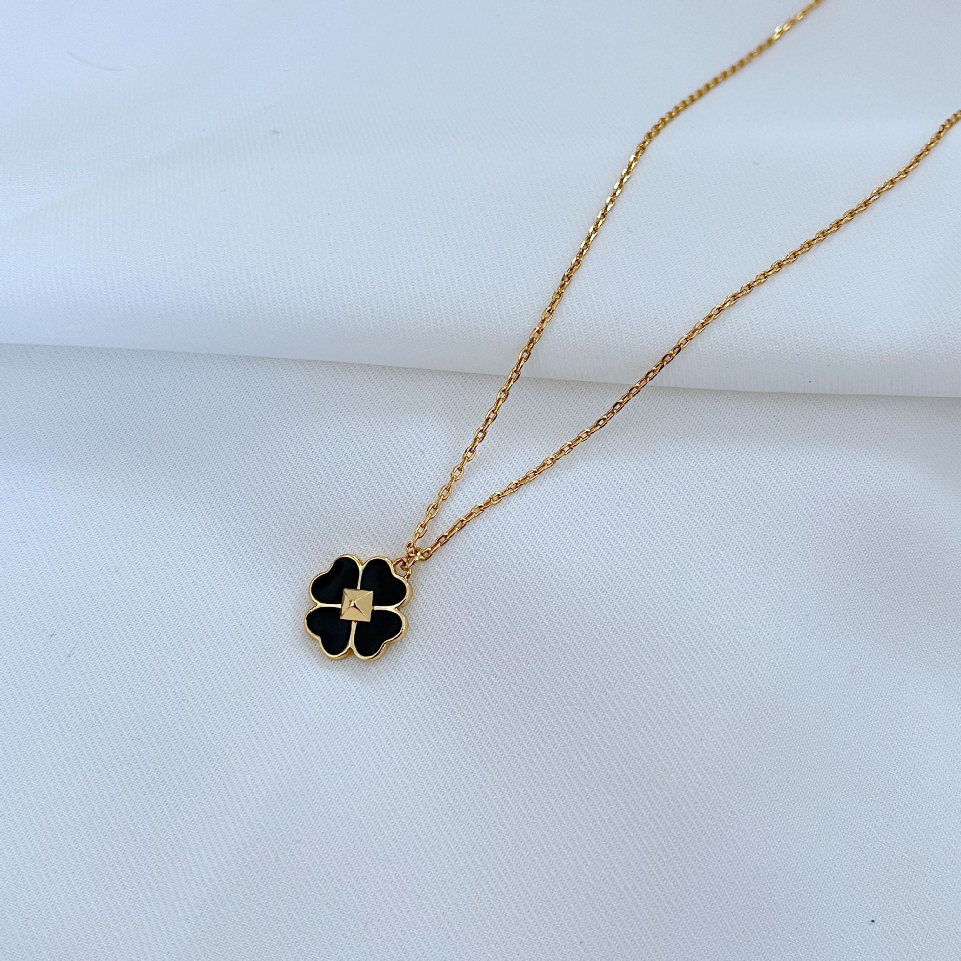 Clean, high-contrast shot of the necklace on a neutral background, highlighting the graphic interplay of gold and black on the clover.