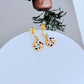 Earrings on a soft pastel pink or cream background, showcasing the donut and coffee charms dangling from huggie hoops. Alt: “Kate Spade Coffee Break Donut Huggies – Enamel Food Jewelry.”