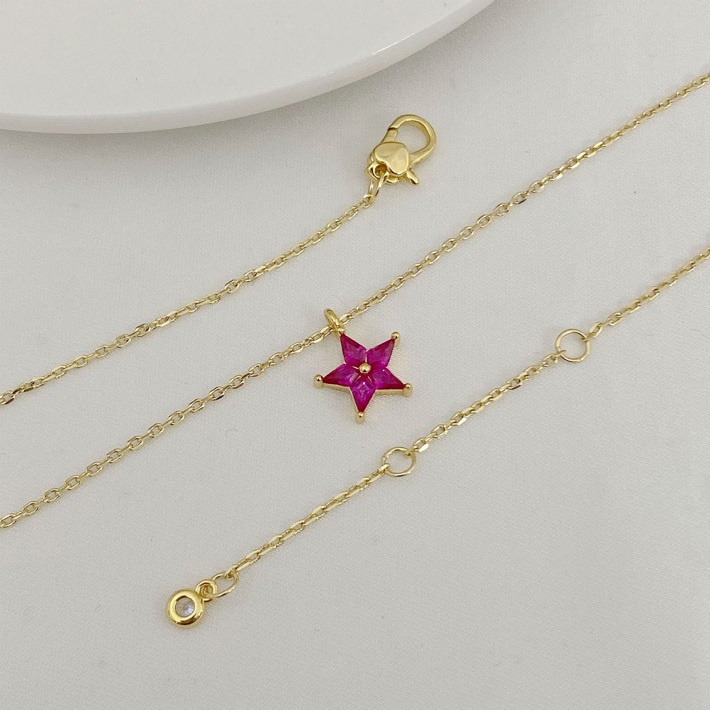 Gold necklace with a star-shaped pink gemstone pendant on a light gray background