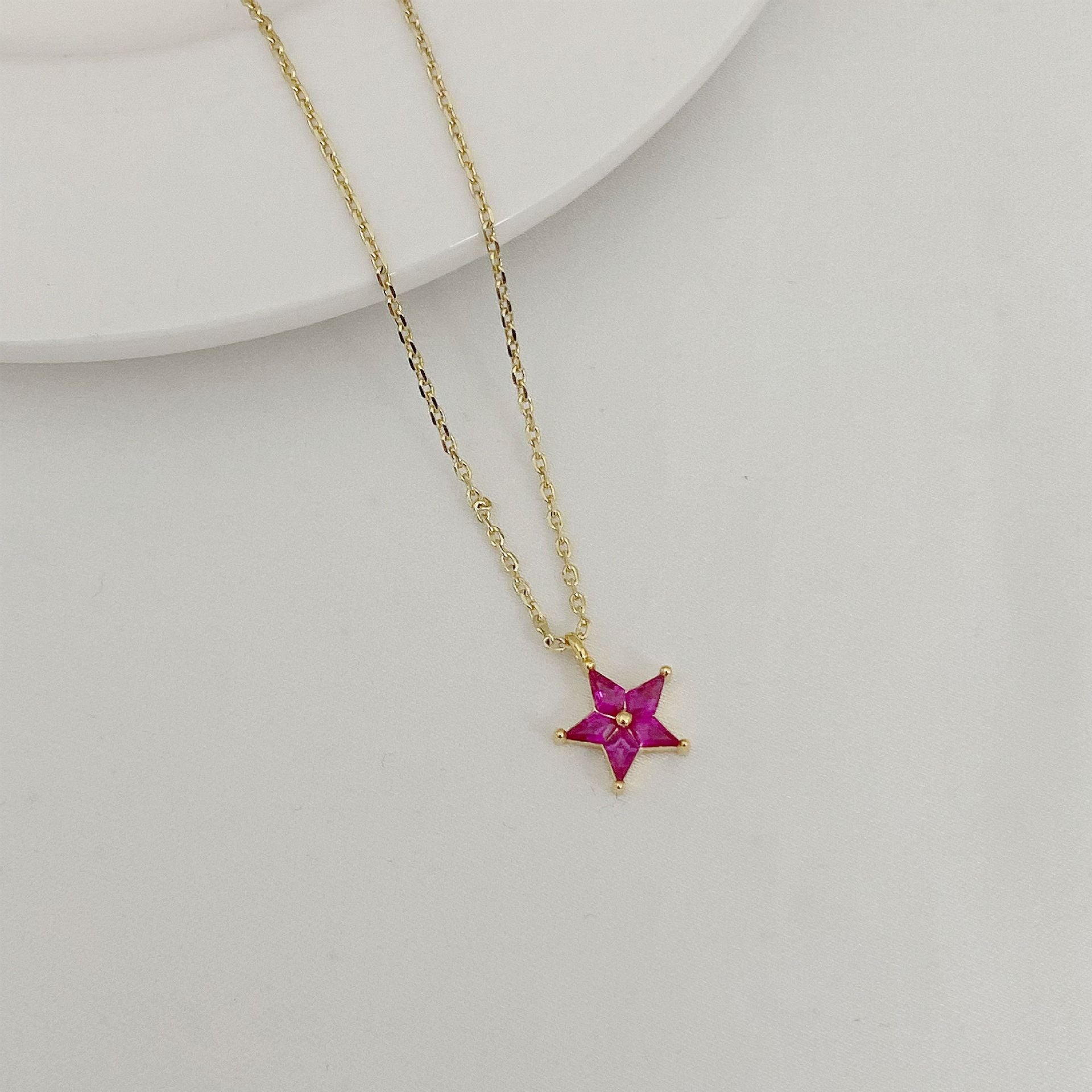 Gold necklace with a star-shaped pendant featuring a red gemstone on a light gray background