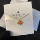 Gold necklace with orange pendant on a Kate Spade card
