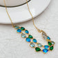 Necklace laid flat on a light neutral background, highlighting the gold setting and vibrant blue/green gemstones. Alt: “Kate Spade Gold Necklace with Blue and Green Gemstones – Colorful Pendant Jewelry.