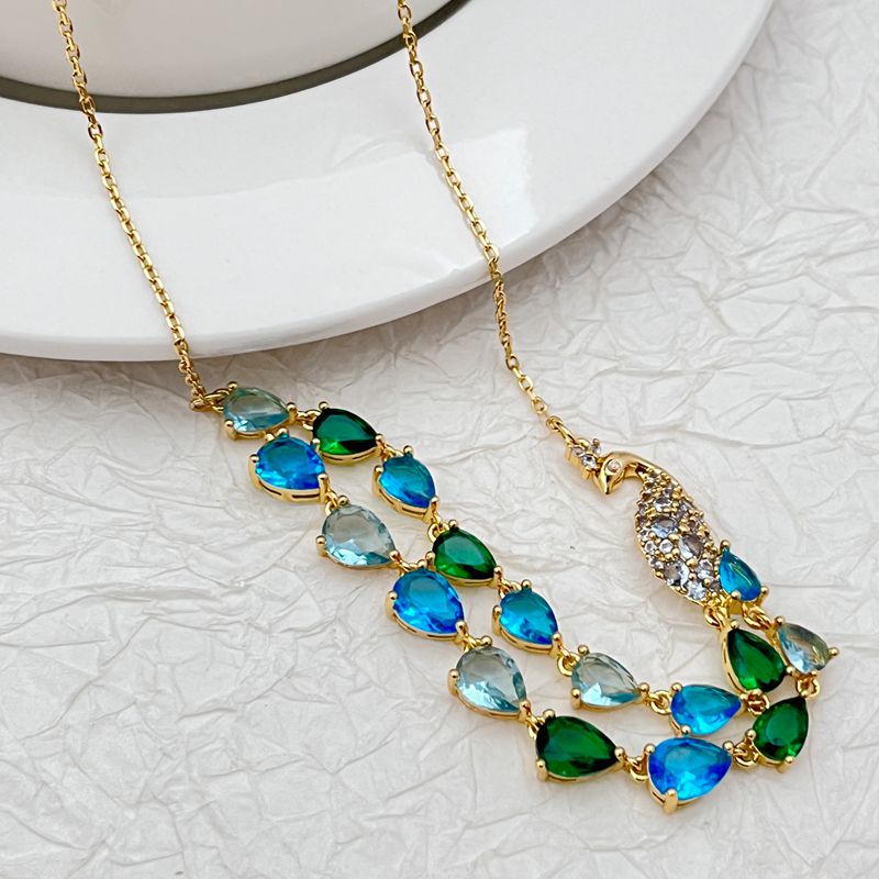 Necklace laid flat on a light neutral background, highlighting the gold setting and vibrant blue/green gemstones. Alt: “Kate Spade Gold Necklace with Blue and Green Gemstones – Colorful Pendant Jewelry.