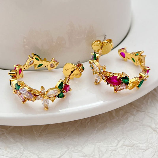 Earrings on a soft moss green or blush pink background, highlighting the floral enamel details along the gold hoop. Alt: “Kate Spade Greenhouse Flora Hoops Earrings – Floral Enamel Hoop Jewelry.”