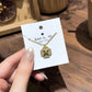 Clean white or soft pastel background — the Kate Spade Heritage Bloom mini pendant displayed on a bust form. The floral enamel pendant catches soft light, showing delicate petal details and the signature Kate Spade aesthetic.