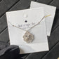 Clean white or soft pastel background — the Kate Spade Heritage Bloom mini pendant displayed on a bust form. The floral enamel pendant catches soft light, showing delicate petal details and the signature Kate Spade aesthetic.