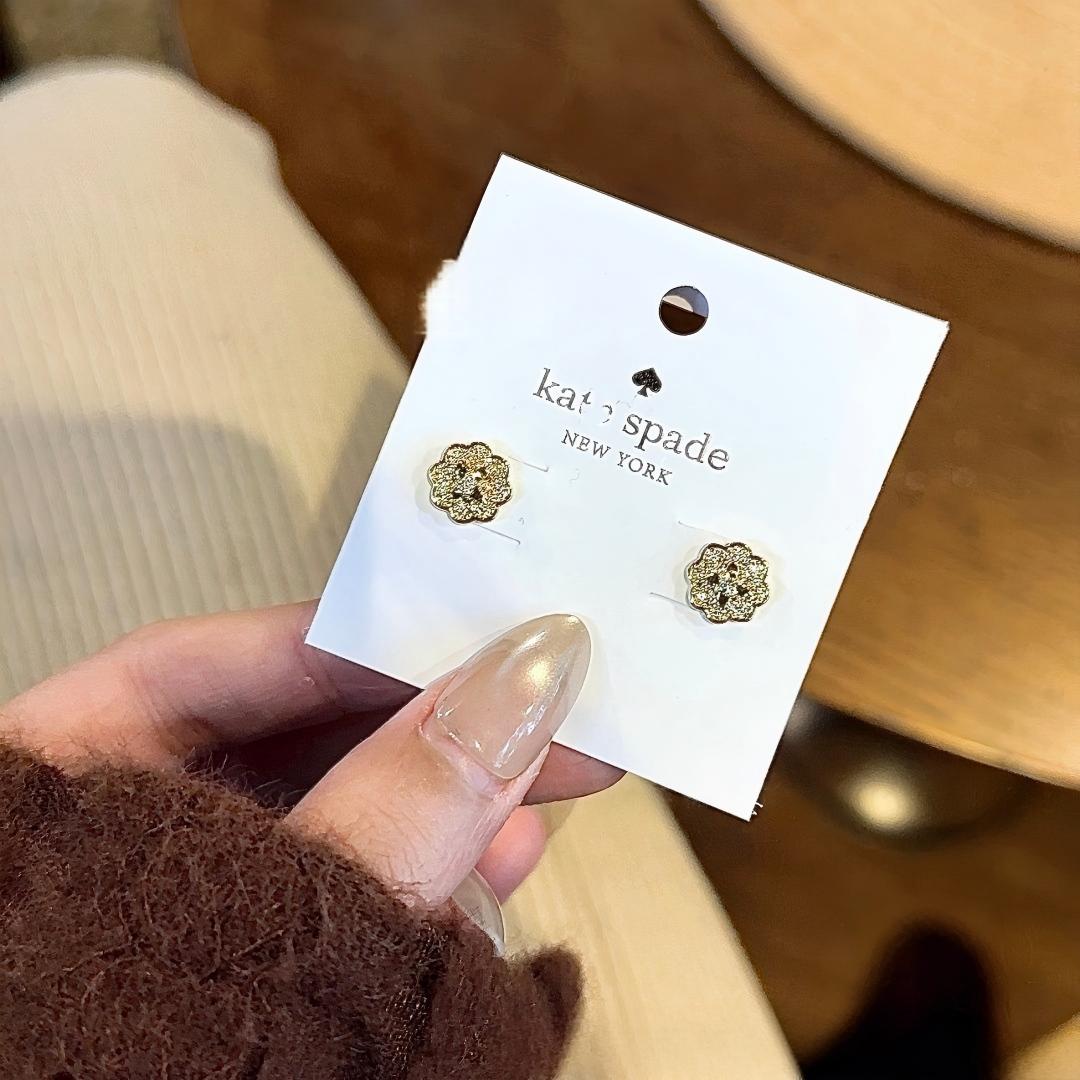 Gold floral earrings on a 'kate spade New York' card held by a hand.