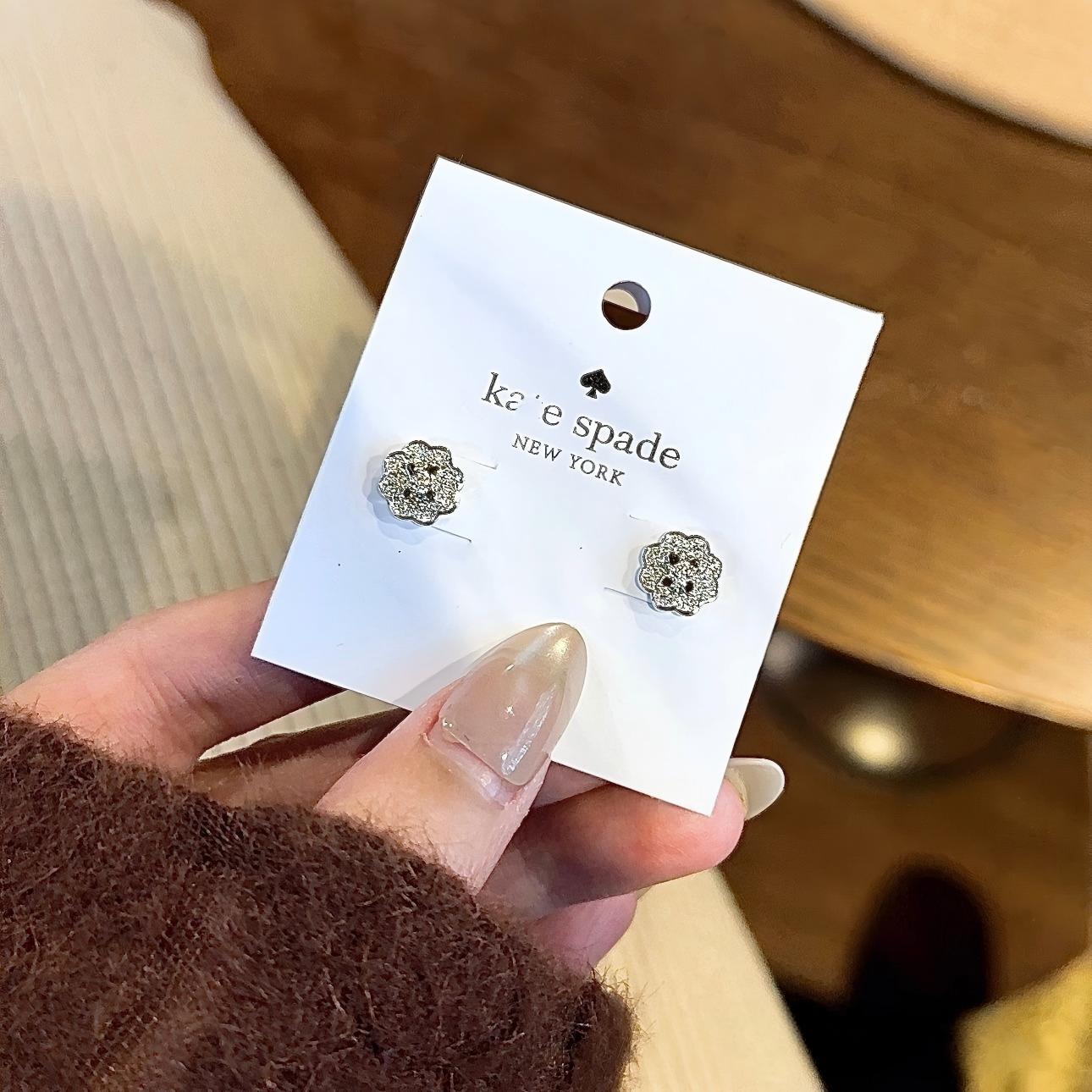 Pair of silver earrings on a Kate Spade card held by a hand.