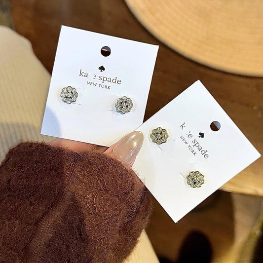 Pair of Kate Spade earrings on display with a hand holding them.