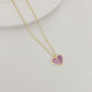 Gold necklace with a heart-shaped pendant featuring pink stones on a light gray background
