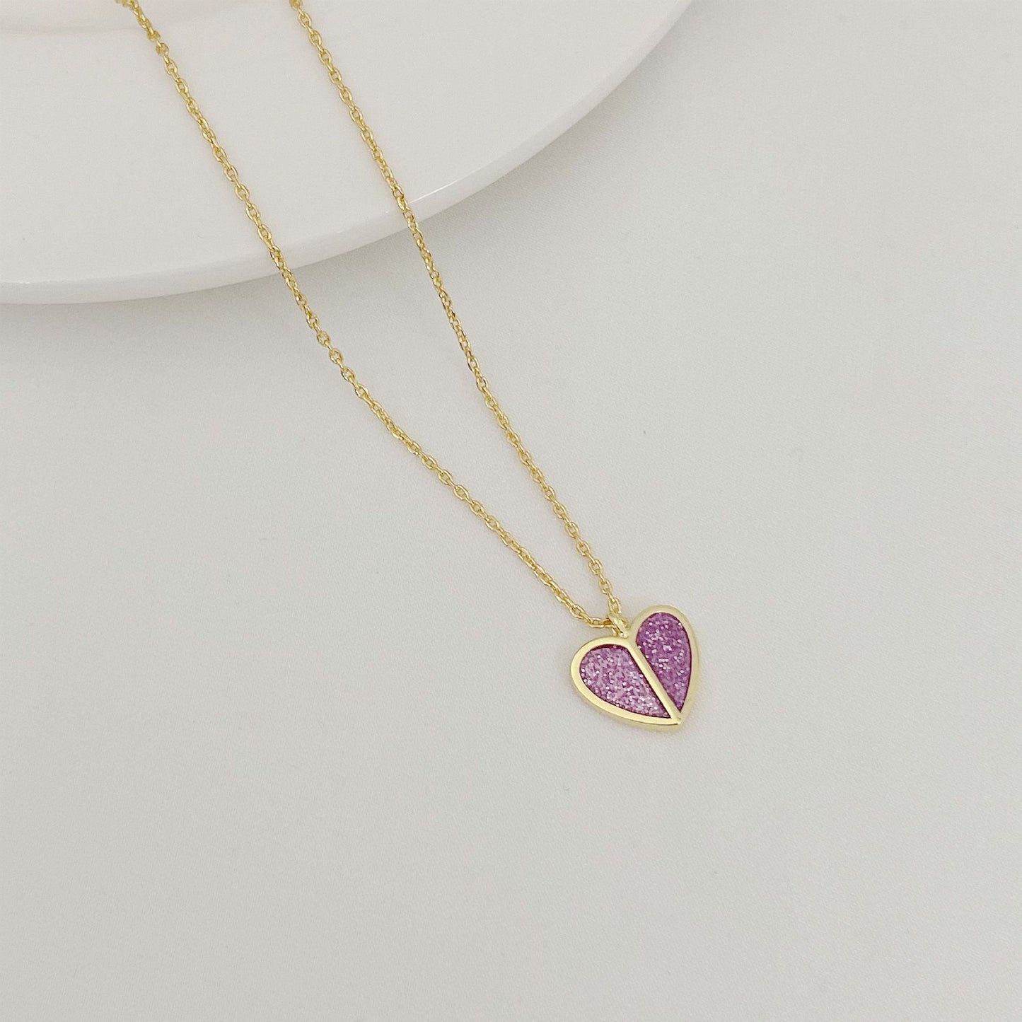 Gold necklace with a heart-shaped pendant featuring pink stones on a light gray background