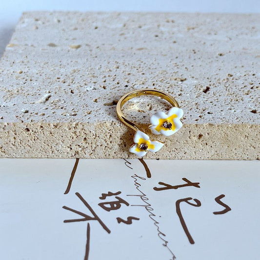 Ring on soft pink background. Alt: “Kate Spade New White Flower Ring – Enamel Floral Jewelry.”