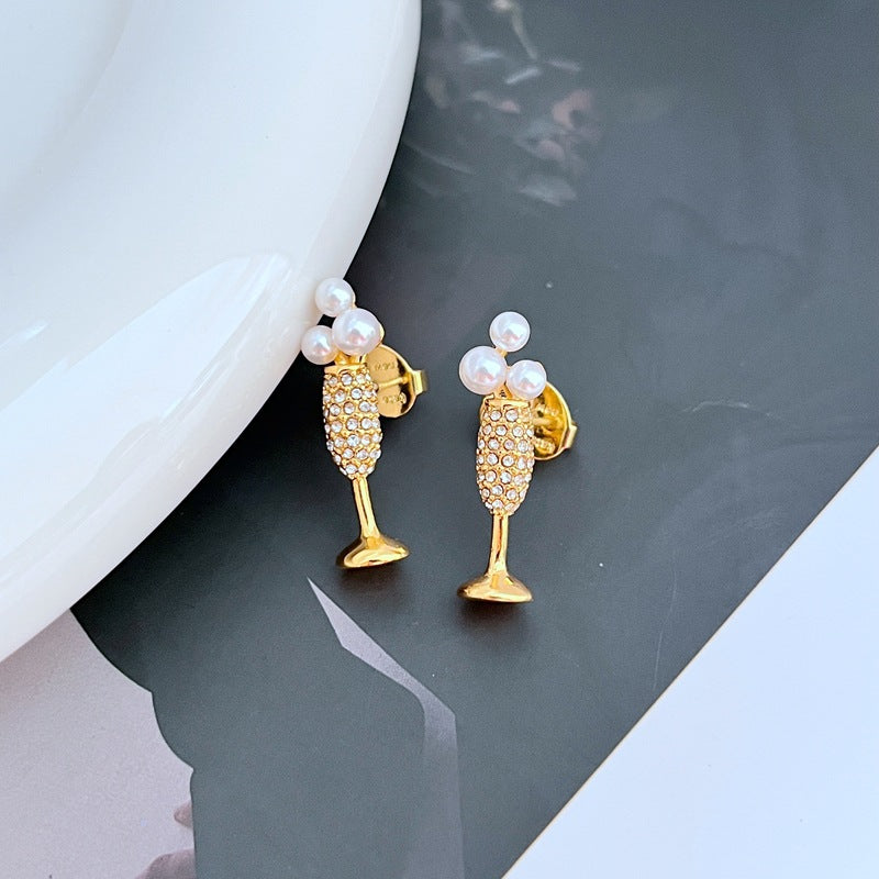 Earrings on a soft gold or champagne-colored background, showcasing the miniature flute shape with crystal bubble. Alt: “Kate Spade New York Champagne Glass Stud Earrings – Gold Flute Celebration Jewelry.”