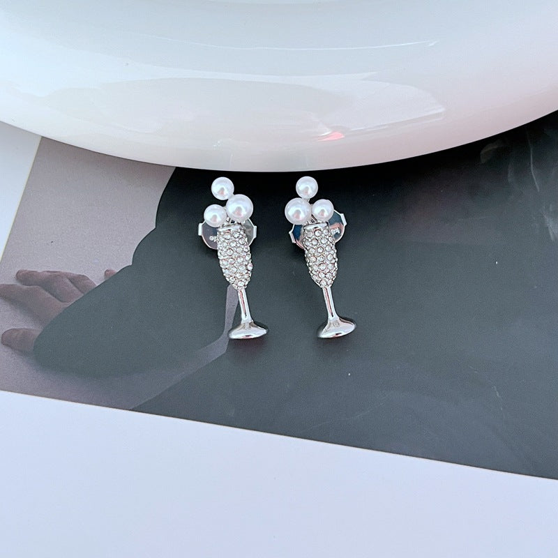 Earrings on a soft gold or champagne-colored background, showcasing the miniature flute shape with crystal bubble. Alt: “Kate Spade New York Champagne Glass Stud Earrings – Gold Flute Celebration Jewelry.”