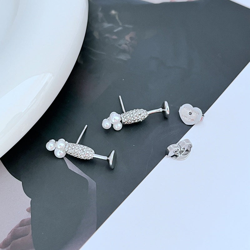 Earrings on a soft gold or champagne-colored background, showcasing the miniature flute shape with crystal bubble. Alt: “Kate Spade New York Champagne Glass Stud Earrings – Gold Flute Celebration Jewelry.”