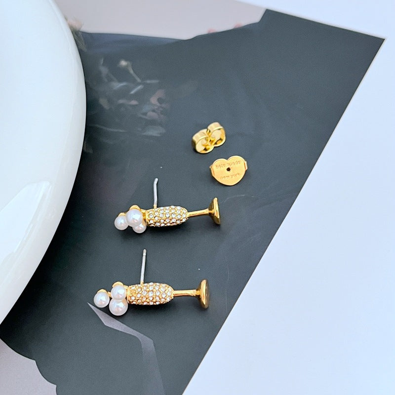 Earrings on a soft gold or champagne-colored background, showcasing the miniature flute shape with crystal bubble. Alt: “Kate Spade New York Champagne Glass Stud Earrings – Gold Flute Celebration Jewelry.”
