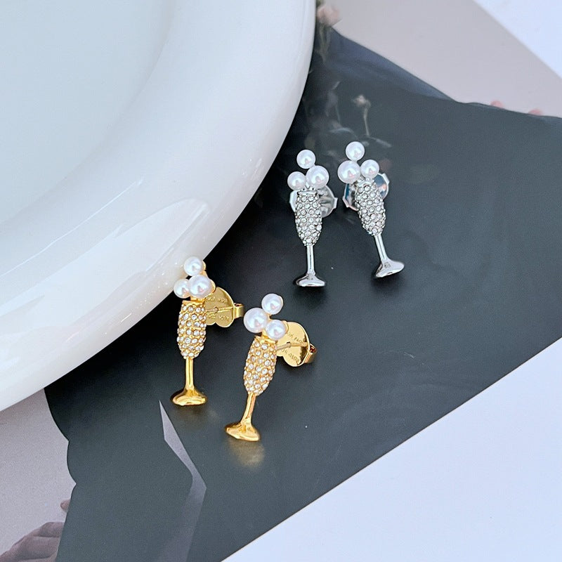 Earrings on a soft gold or champagne-colored background, showcasing the miniature flute shape with crystal bubble. Alt: “Kate Spade New York Champagne Glass Stud Earrings – Gold Flute Celebration Jewelry.”