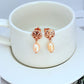 Earrings on a soft sand-beige or seafoam green background, highlighting the warm pink conch pearl and gold setting. Alt: “Kate Spade New York Conch Pearl Gold Tone Earrings – Shell Pearl Drop Jewelry.”