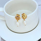 Earrings on a soft sand-beige or seafoam green background, highlighting the warm pink conch pearl and gold setting. Alt: “Kate Spade New York Conch Pearl Gold Tone Earrings – Shell Pearl Drop Jewelry.”