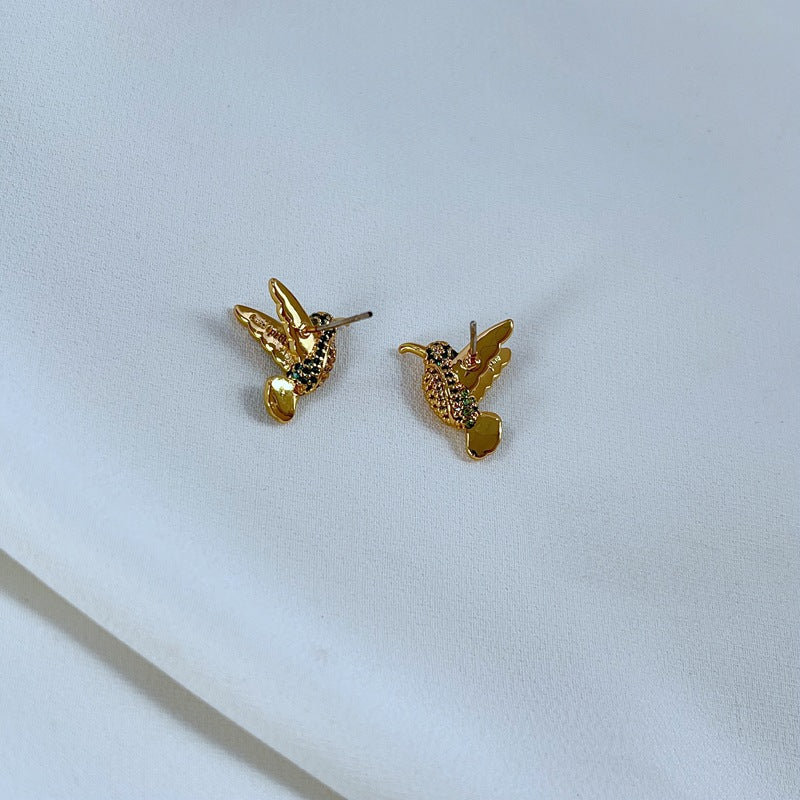 Earrings on a soft sage green or misty blue background, showcasing the hummingbird charm with iridescent enamel wings. Alt: “Kate Spade New York Hummingbird Earrings – Enamel Bird Drop Jewelry.”