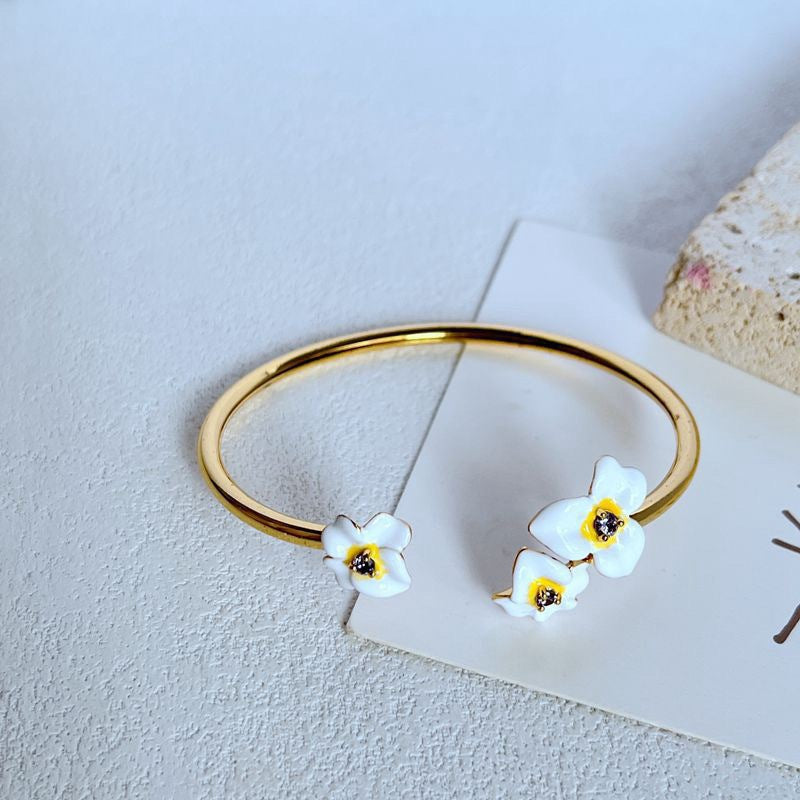 Cuff on a soft cream or dusty rose background, showcasing the purple and gold pansy enamel detail. Alt: “Kate Spade New York Precious Pansy Enamel Cuff – Purple Floral Bracelet.”