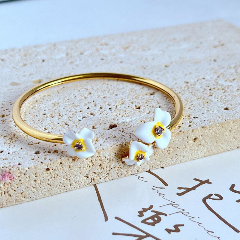 Cuff on a soft cream or dusty rose background, showcasing the purple and gold pansy enamel detail. Alt: “Kate Spade New York Precious Pansy Enamel Cuff – Purple Floral Bracelet.”