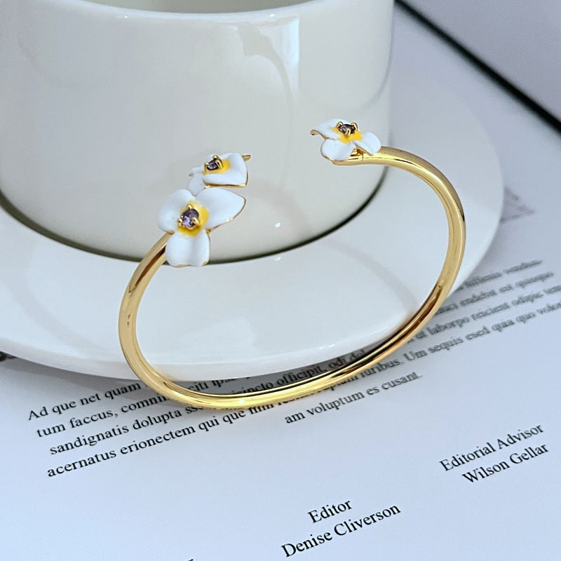 Cuff on a soft cream or dusty rose background, showcasing the purple and gold pansy enamel detail. Alt: “Kate Spade New York Precious Pansy Enamel Cuff – Purple Floral Bracelet.”