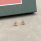 Pink stud earrings on a gray surface with a green box in the background