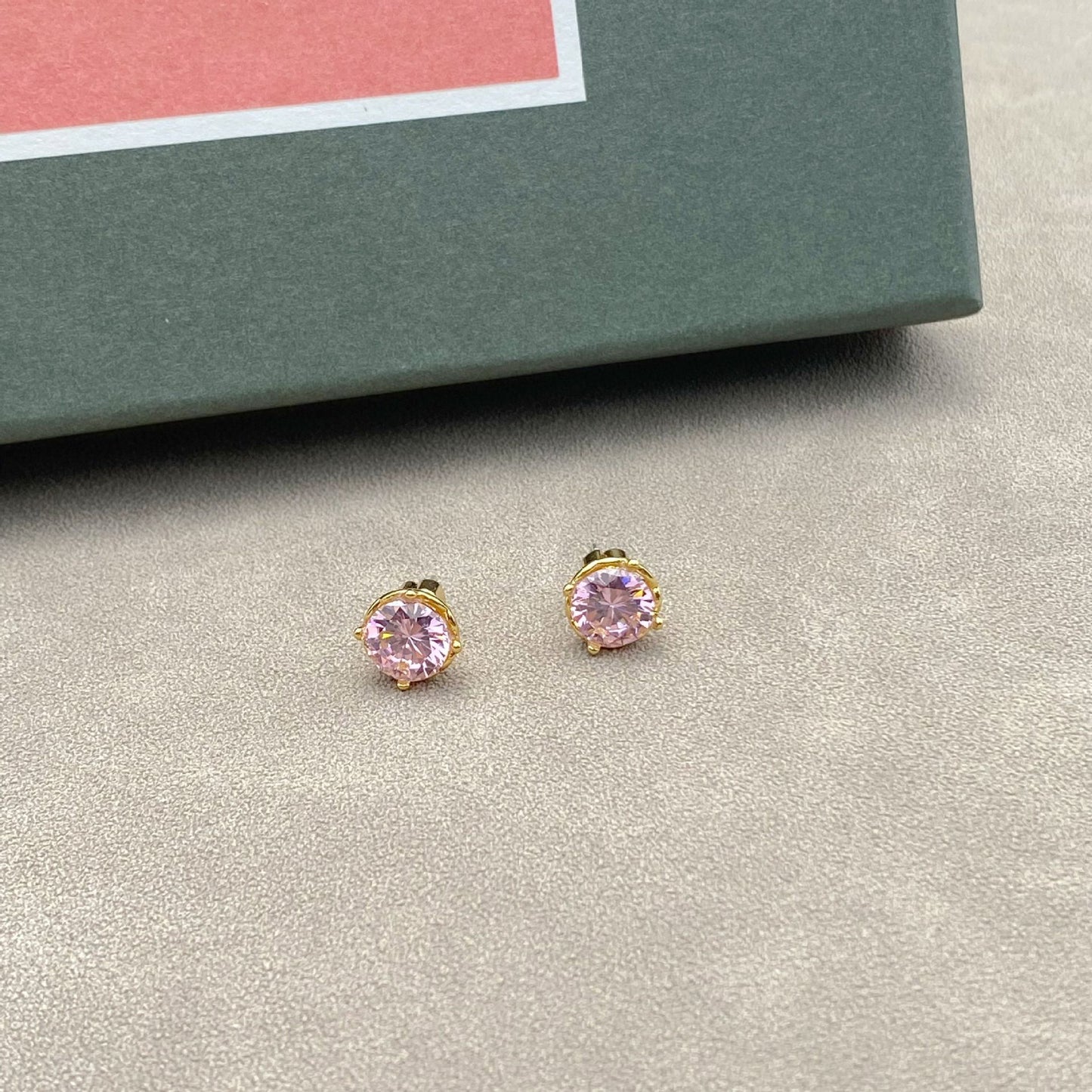 Pink stud earrings on a gray surface with a green box in the background