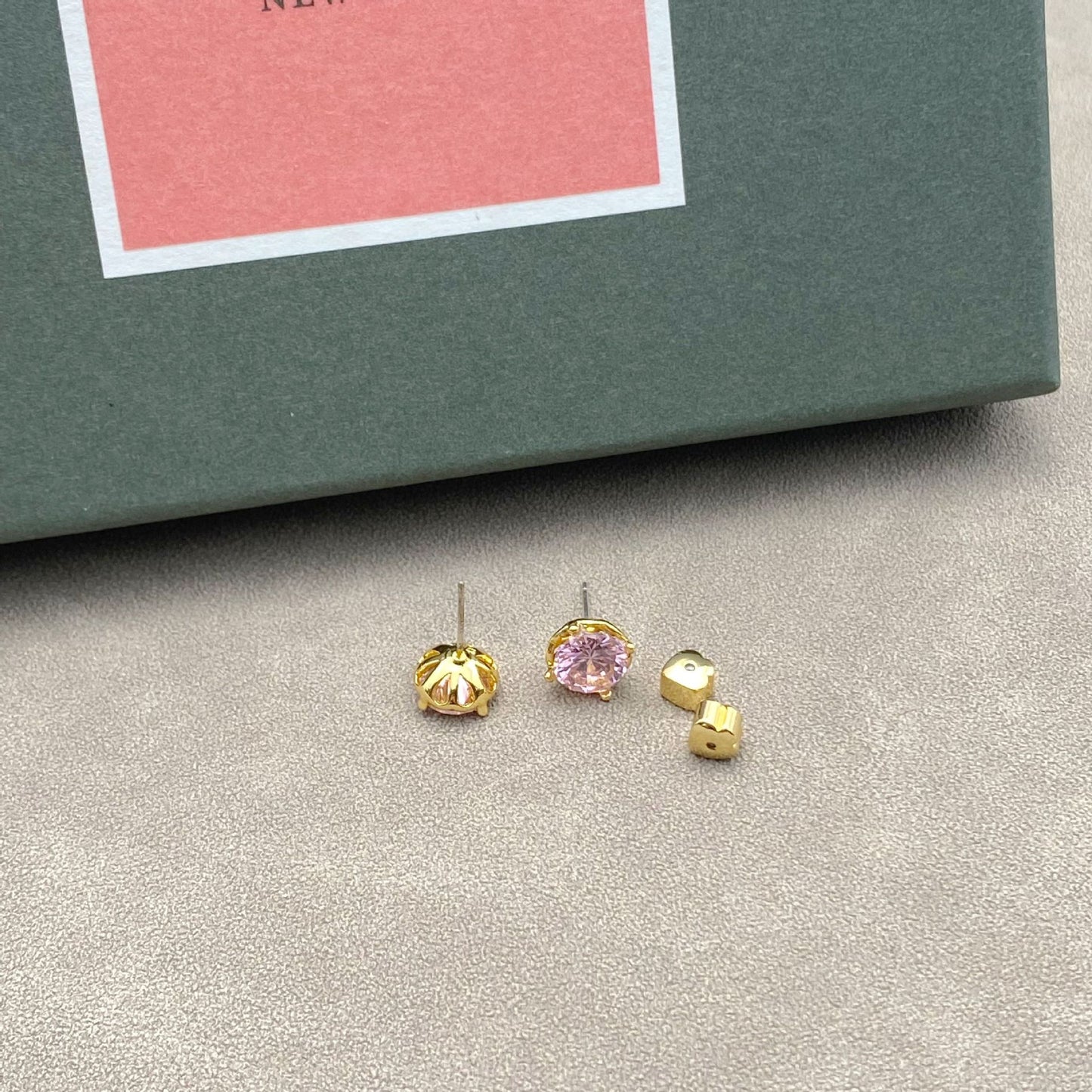Three gold earrings with different gemstones on a gray surface.