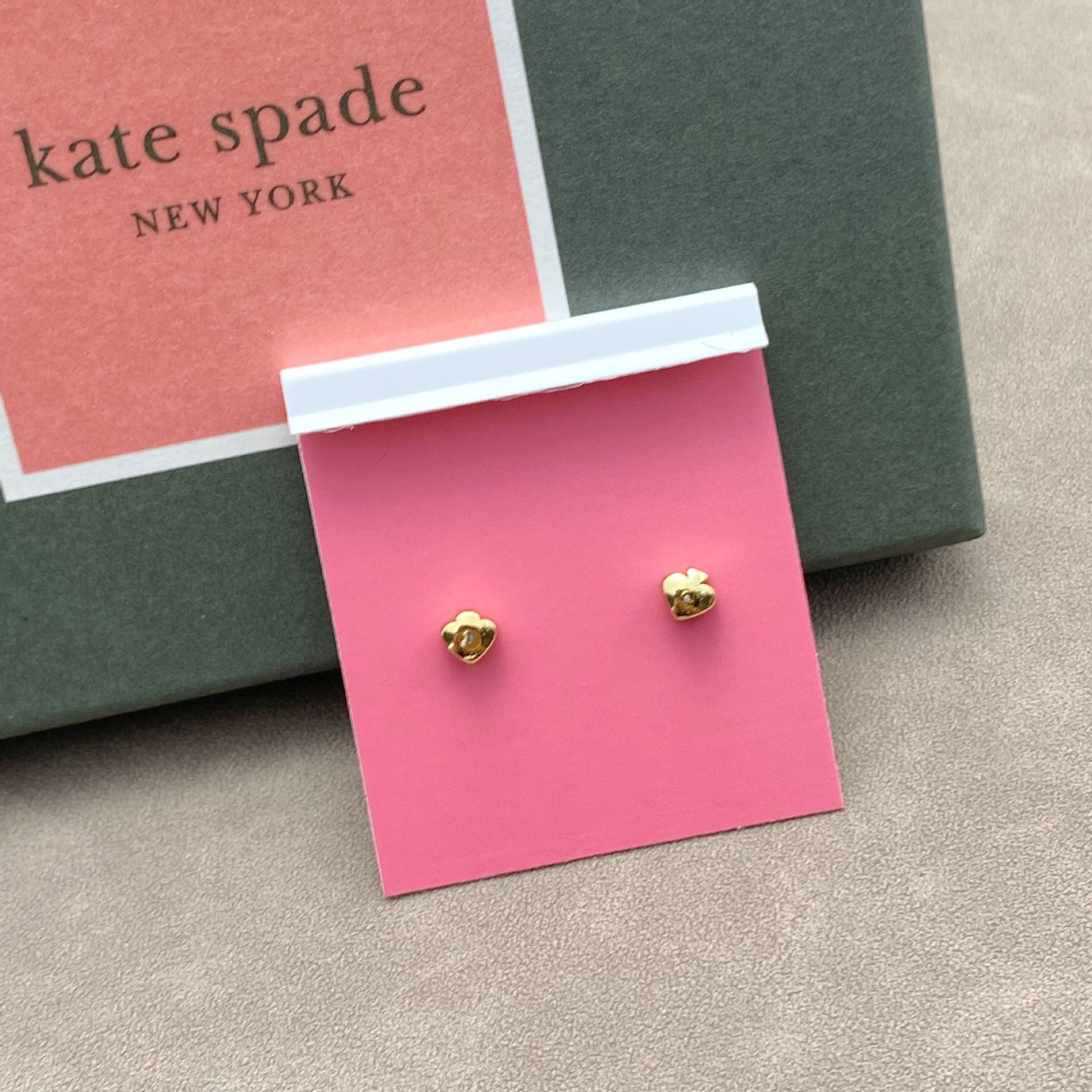 Gold earrings on a pink card with 'kate spade New York' branding in the background.