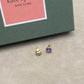 Gold and purple earrings on a gray surface with a Kate Spade box in the background.