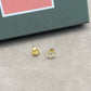 Gold stud earrings on a gray surface with a pink and green box in the background