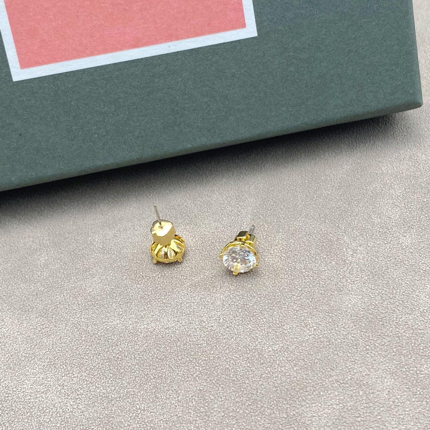 Gold stud earrings on a gray surface with a pink and green box in the background
