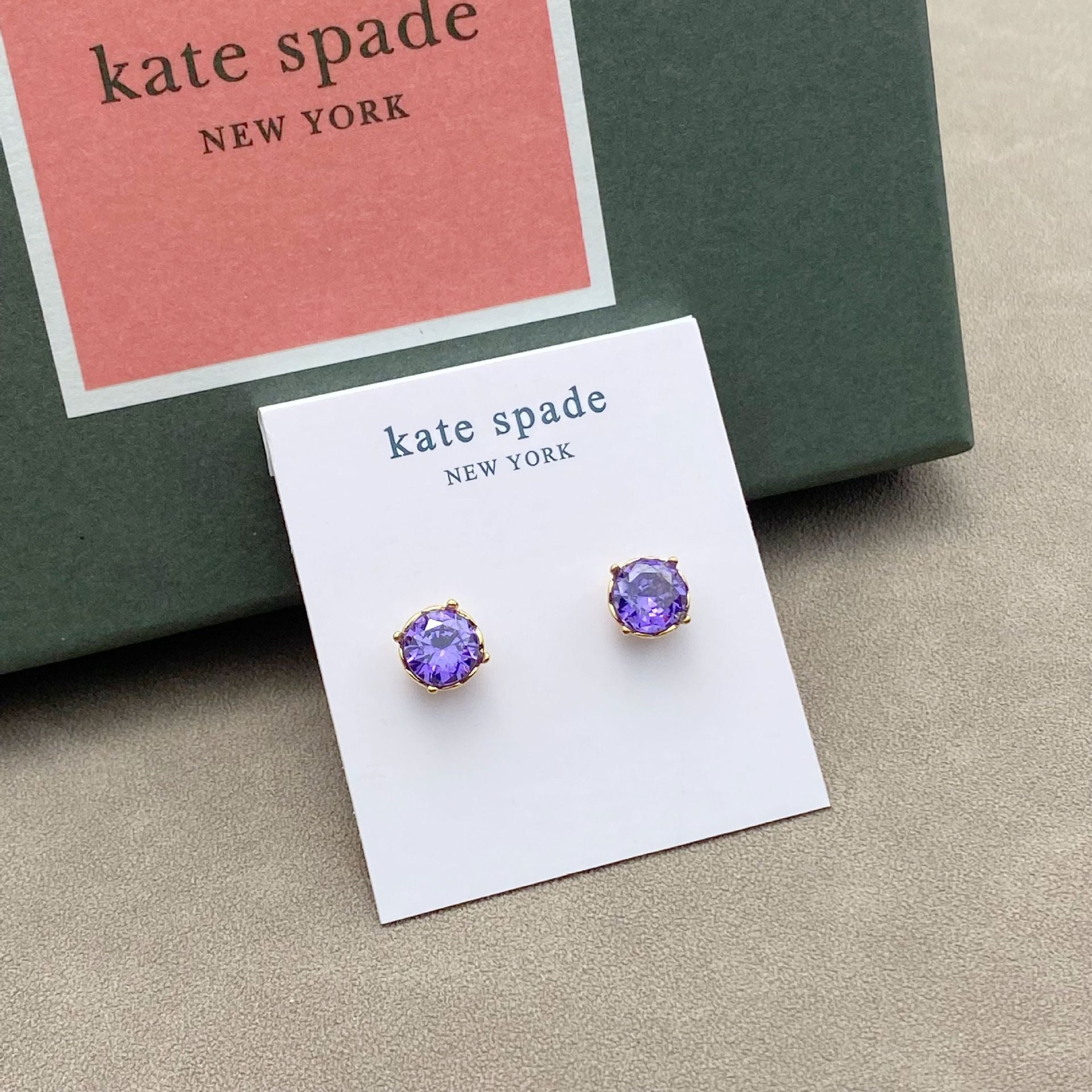 Purple gemstone earrings on a Kate Spade New York card with a green box in the background.